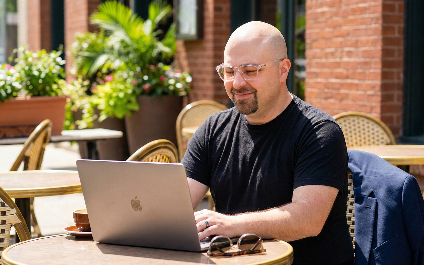 Simon sitting at an outdoor cafe in the morning sun working on his laptop computer